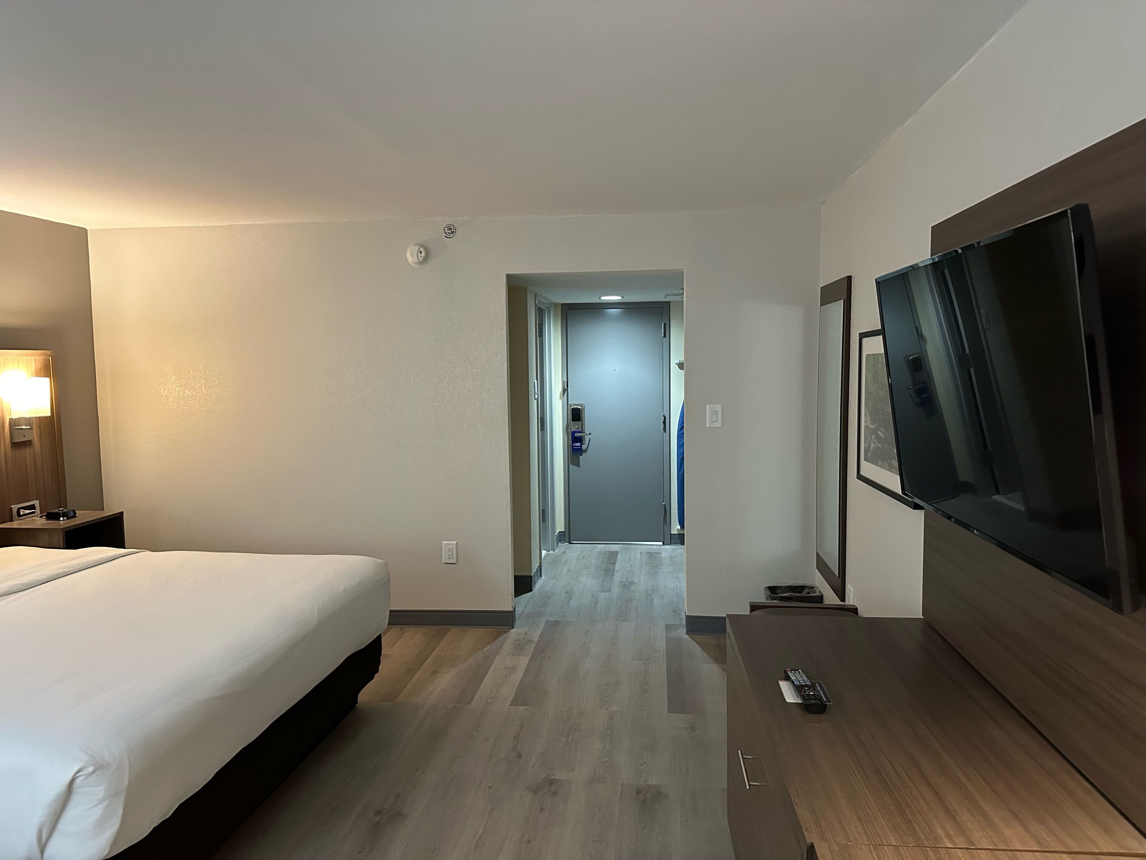 Una habitación de hotel con una cama, televisor, escritorio y puerta que da a un pasillo.