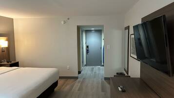 Una habitación de hotel con una cama, televisor, escritorio y puerta que da a un pasillo.