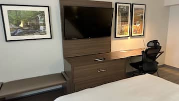 Quarto de hotel com cama, escrivaninha com cadeira, televisão e quadros na parede.