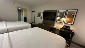 A hotel room with two beds, a desk, a TV, and framed pictures on the wall.