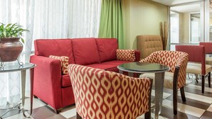 A hotel lobby with a red sofa, patterned armchairs, a round glass table, and a potted plant. - Comfort Inn Conyers (Conyers)