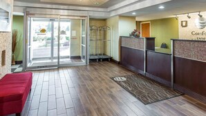 A hotel reception area with a wooden floor, a red bench, a reception desk, and a glass door entrance. - Comfort Inn Conyers (Conyers)
