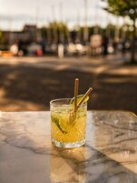 Un vaso de bebida amarilla con una rodaja de lima y dos pajitas sobre una mesa de mármol.