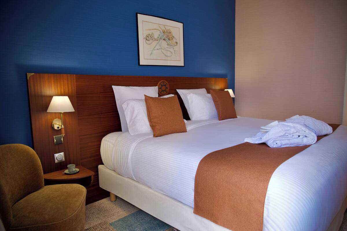 A hotel room with a large bed, a nightstand with a lamp, a chair, and a framed picture on the wall.