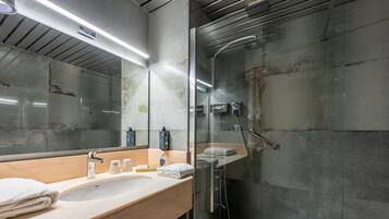 A modern bathroom with a glass shower enclosure, a large mirror, and a vanity with a sink and towel.