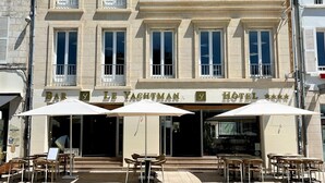Un edificio de varios pisos con bar y restaurante para navegantes en la planta baja, que cuenta con mesas al aire libre y sombrillas.