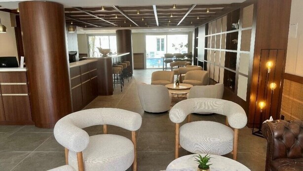 Un moderno vestíbulo de hotel con una recepción, zona de estar y vistas a la piscina.