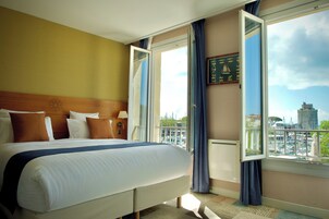 A hotel room with a large bed, a view of the city, and a balcony with curtains.