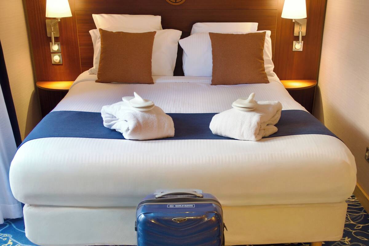 A neatly made bed with pillows, a blue suitcase, and two wall-mounted lamps.