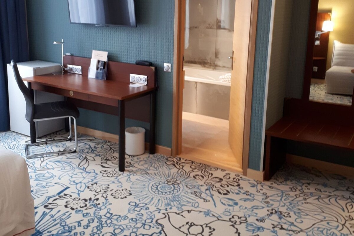 A hotel room with a desk, chair, flat-screen TV, and a bed.