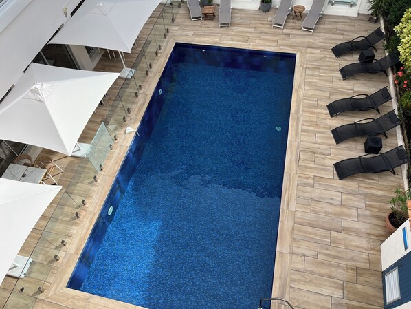 A rectangular pool with a tiled border, surrounded by lounge chairs and umbrellas.