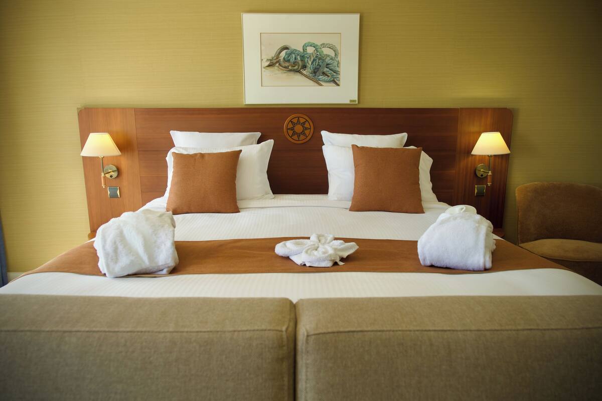 A hotel room with a large bed, two side tables with lamps, a headboard with a decorative plate, and a painting above the bed.