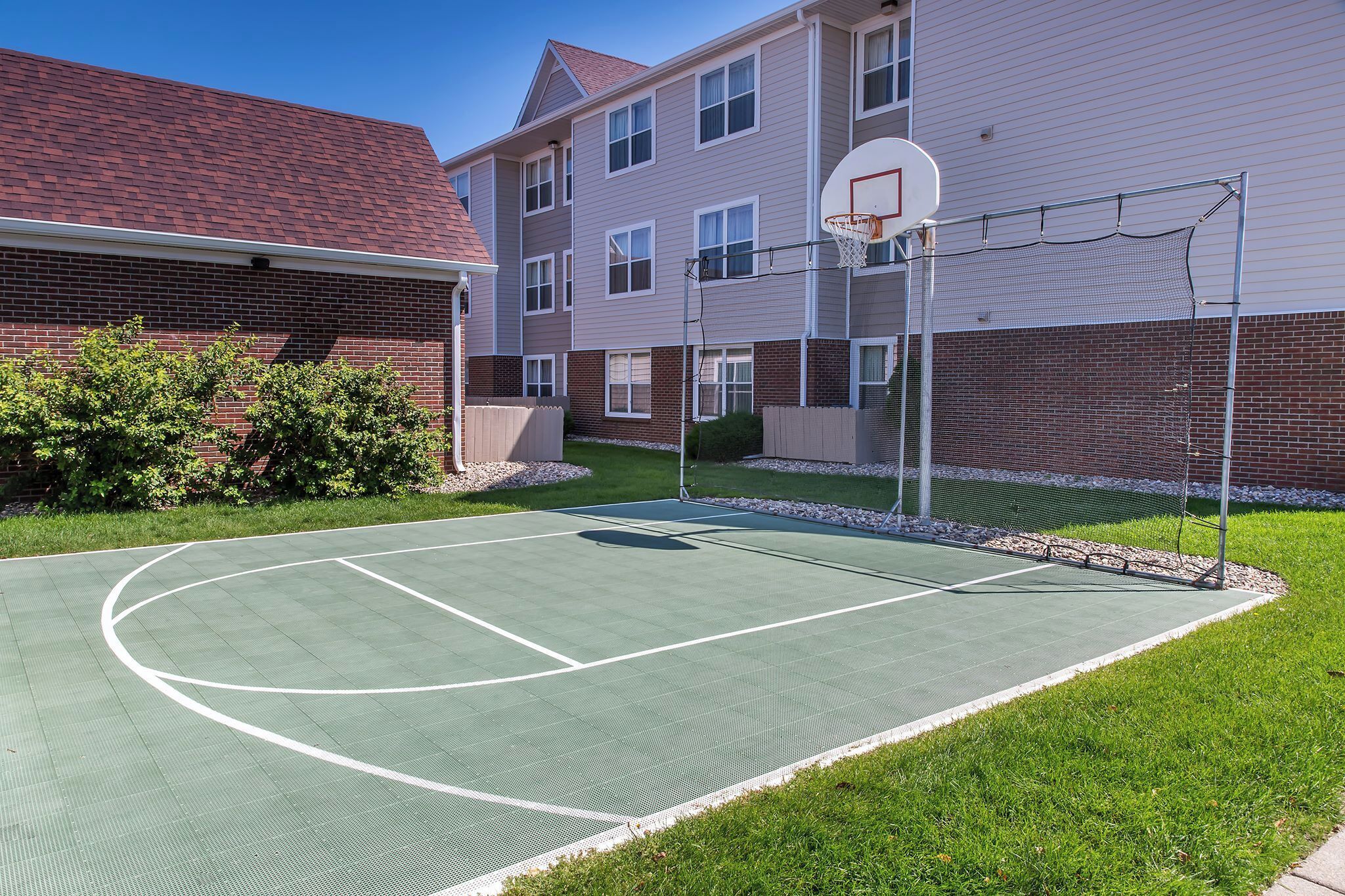 Una cancha de baloncesto al aire libre contigua a un edificio de fachada de ladrillo y múltiples ventanales.