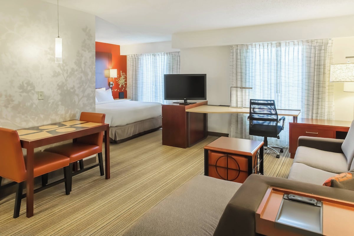 A hotel room with a bed, a desk with a TV, a dining table, and a sofa.