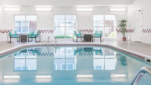An indoor swimming pool with a tiled border, two chairs, a table, and a potted plant. - Residence Inn Sioux Falls (Sioux Falls)