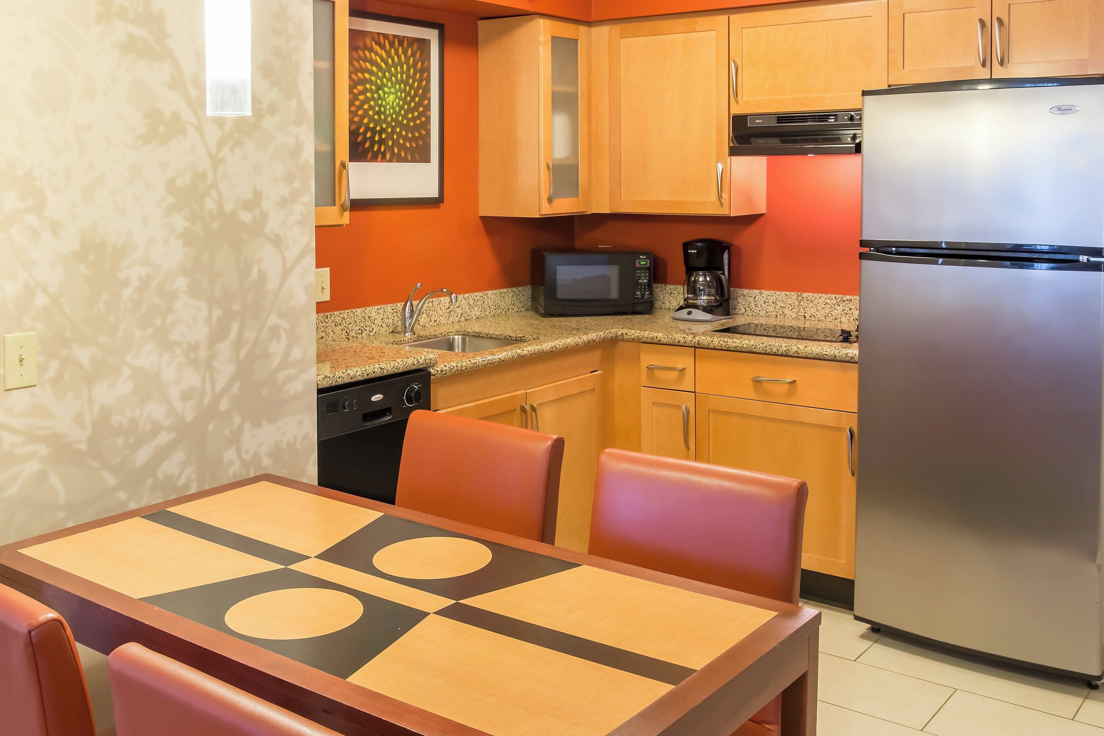 Cocina compacta con armarios de madera, un refrigerador de acero inoxidable, un microondas y una cafetera.