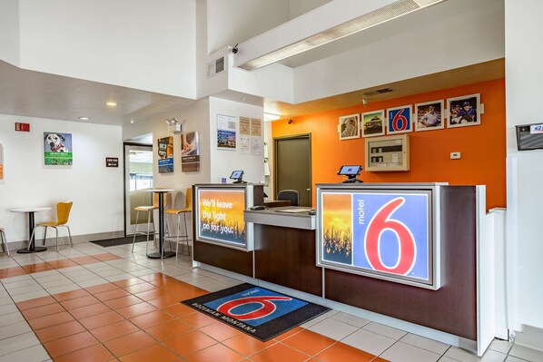 A hotel reception area with a check-in counter, a seating area with chairs, and a reception desk with a digital display.