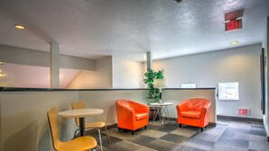 A lobby with a checkered carpet, two orange armchairs, a small round table, and a potted plant.