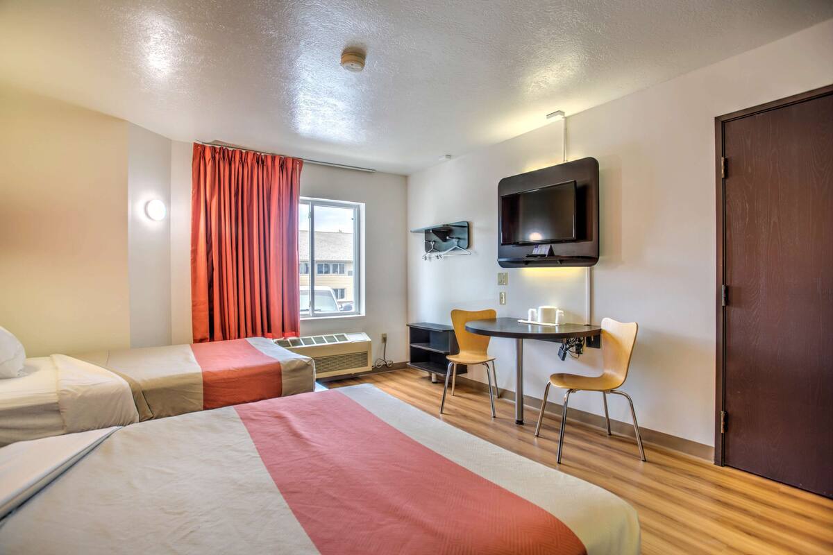 A hotel room with two beds, a desk with a chair, a TV, and a window with curtains.