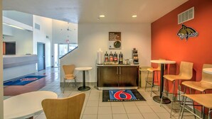 A hotel lobby with a reception desk, a coffee station, and seating areas.