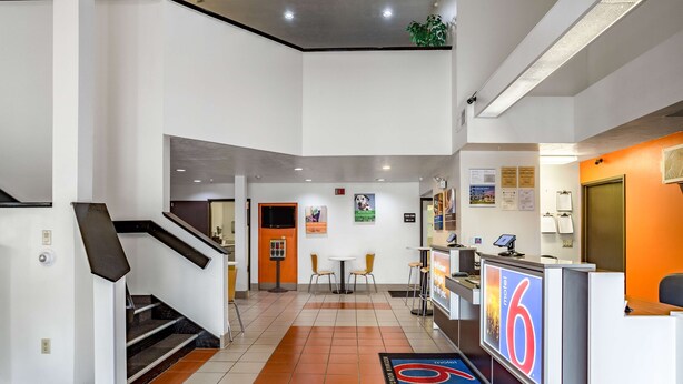 A hotel lobby with a reception desk, a staircase, and a seating area with chairs.