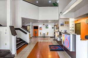 A hotel lobby with a reception desk, a staircase, and a seating area with chairs.