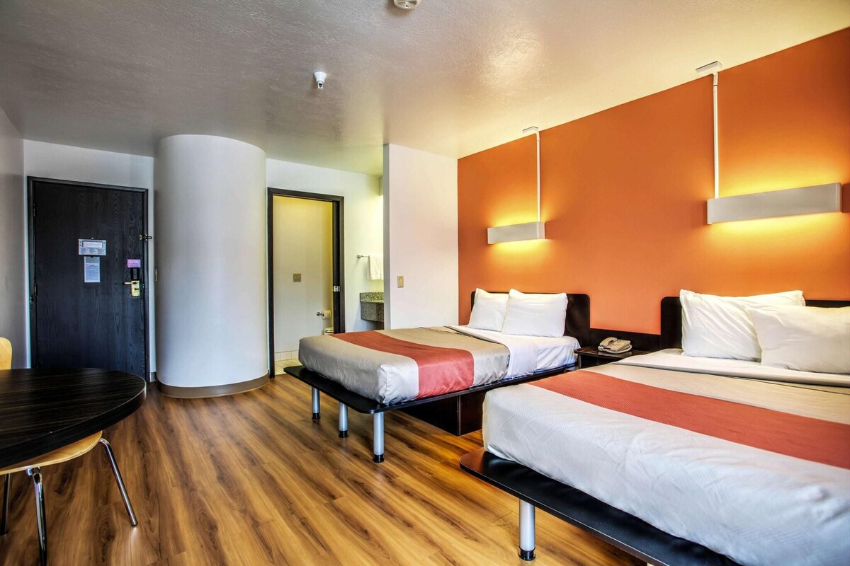 A hotel room with two beds, a desk, and a chair.