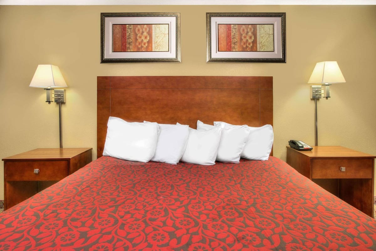 A hotel room with a large bed, two nightstands, two wall-mounted lamps, and two framed artworks above the bed.