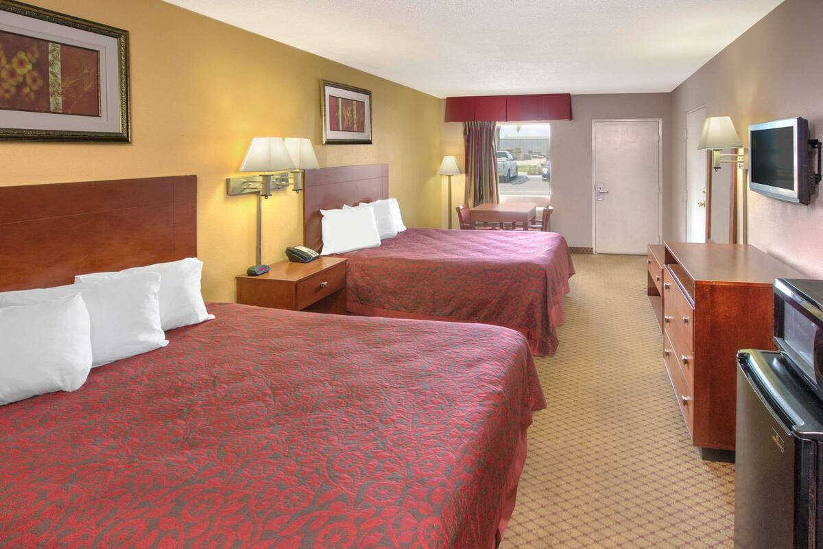 A hotel room with two beds, a desk, a chair, a television, and a dresser.