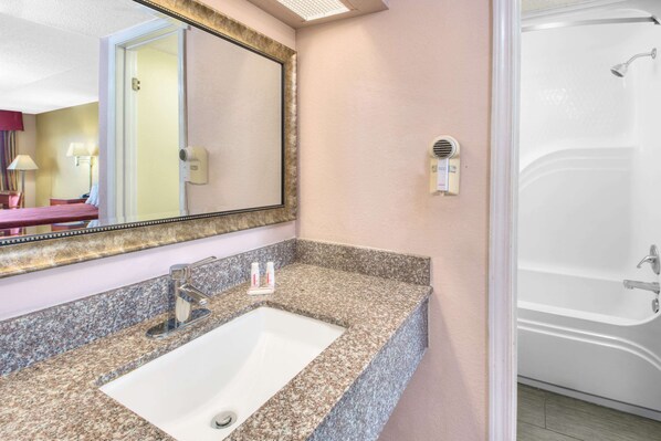 A bathroom with a granite countertop sink, a large mirror, and a white bathtub.