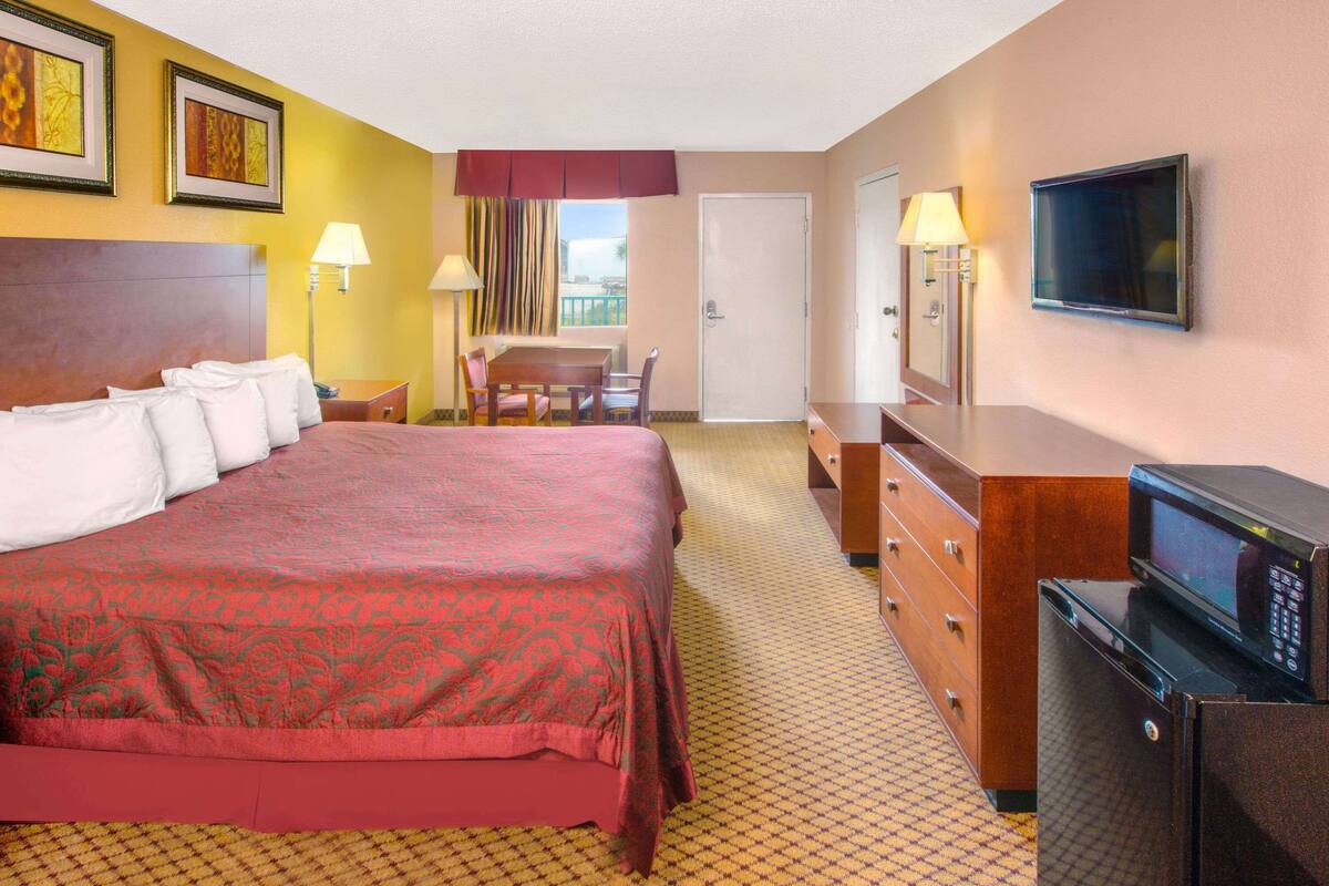 A hotel room with a large bed, a desk, a chair, a television, and a microwave.