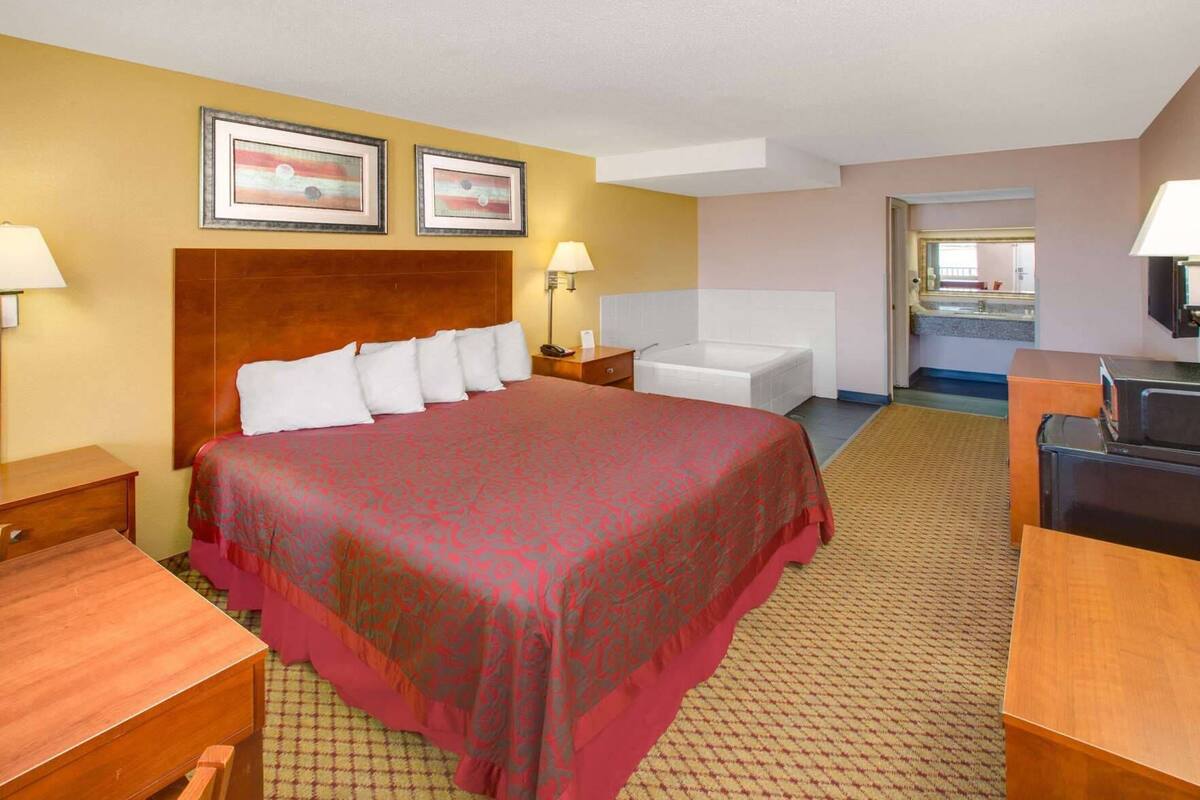 A hotel room with a large bed, a desk, a chair, a nightstand, a bathroom with a bathtub, and a television.