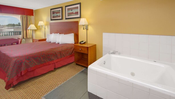 A hotel room with a large bed, a bathtub, and two framed pictures on the wall. - Days Inn by Wyndham Gulfport (Gulfport)