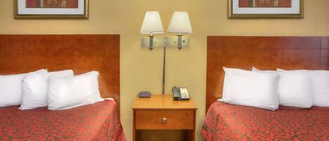 A hotel room with two beds, a nightstand with a lamp, a phone, and framed artwork on the walls.