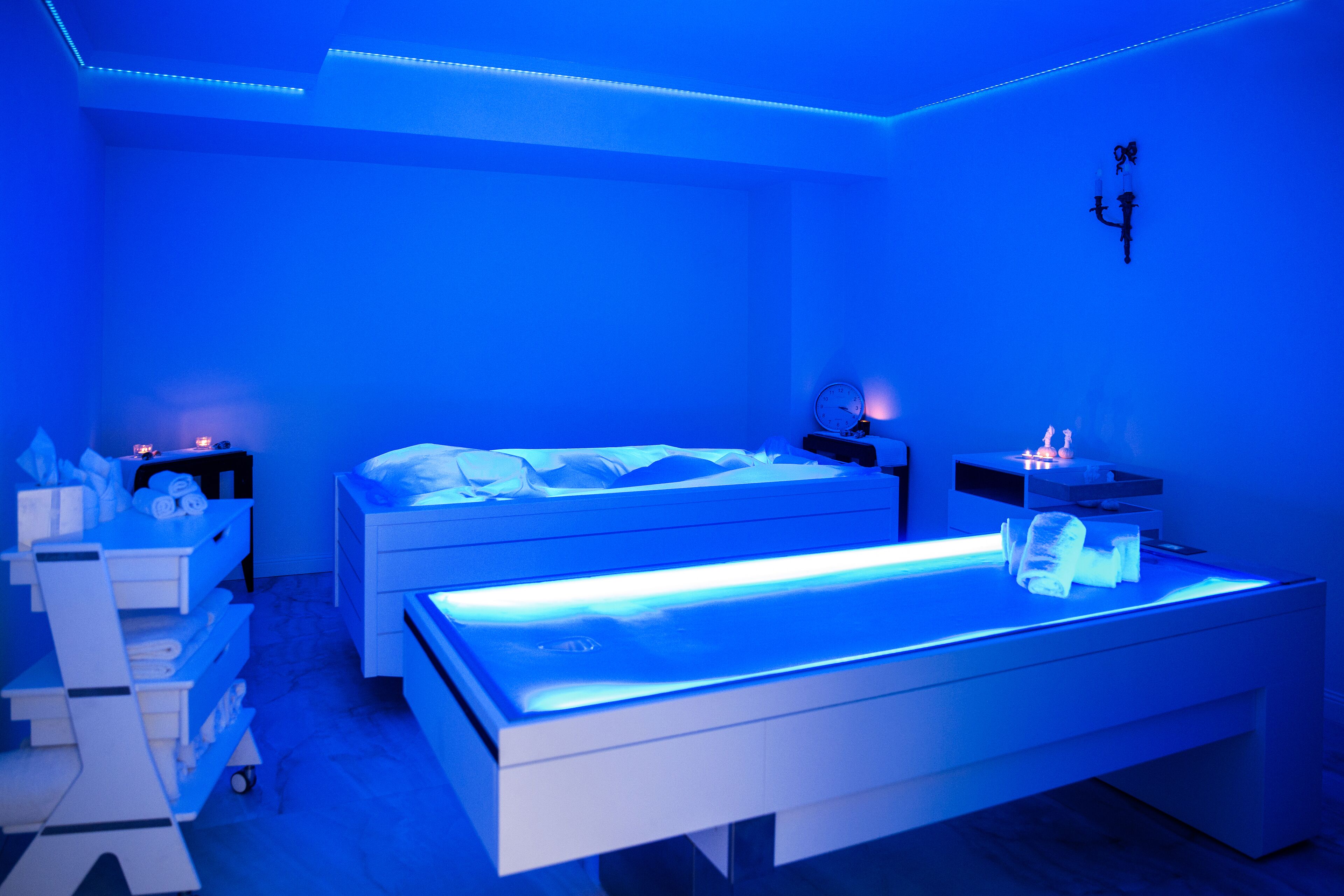 Ein modernes Schlafzimmer mit zwei Betten, einer Massageliege und einem Nachttisch mit Lampe.