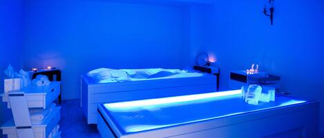 A modern bedroom with two beds, a massage table, and a nightstand with a lamp.