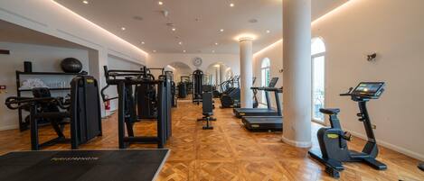 A spacious gym with various exercise equipment, including treadmills and weight machines, and a polished wooden floor.
