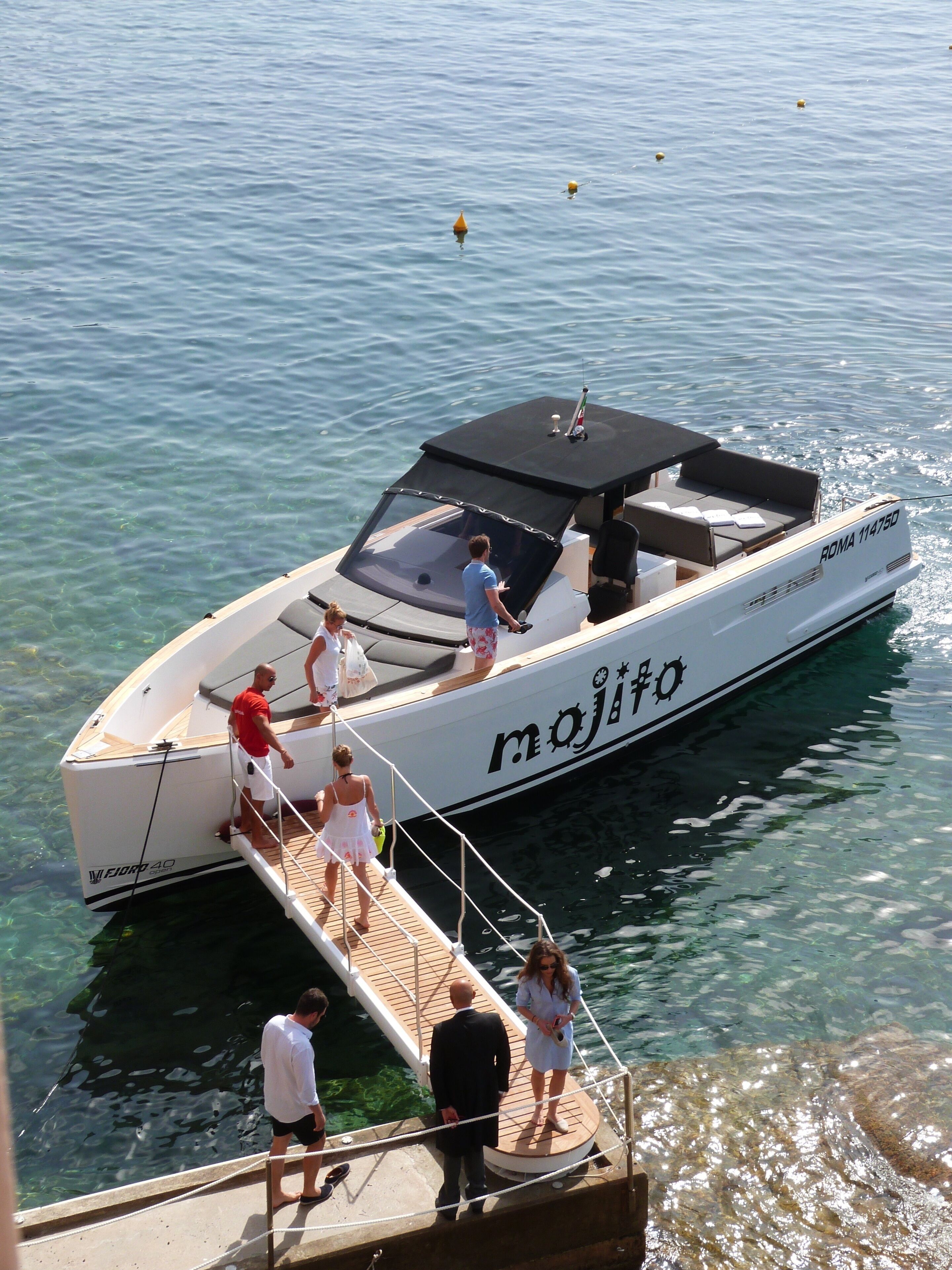 Un bateau doté d’un pont couvert et portant le nom « Mojito » sur sa coque était amarré à un quai, dans une eau cristalline.