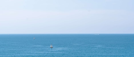 A coastal view with a clear sky, calm sea, and distant sailboats.