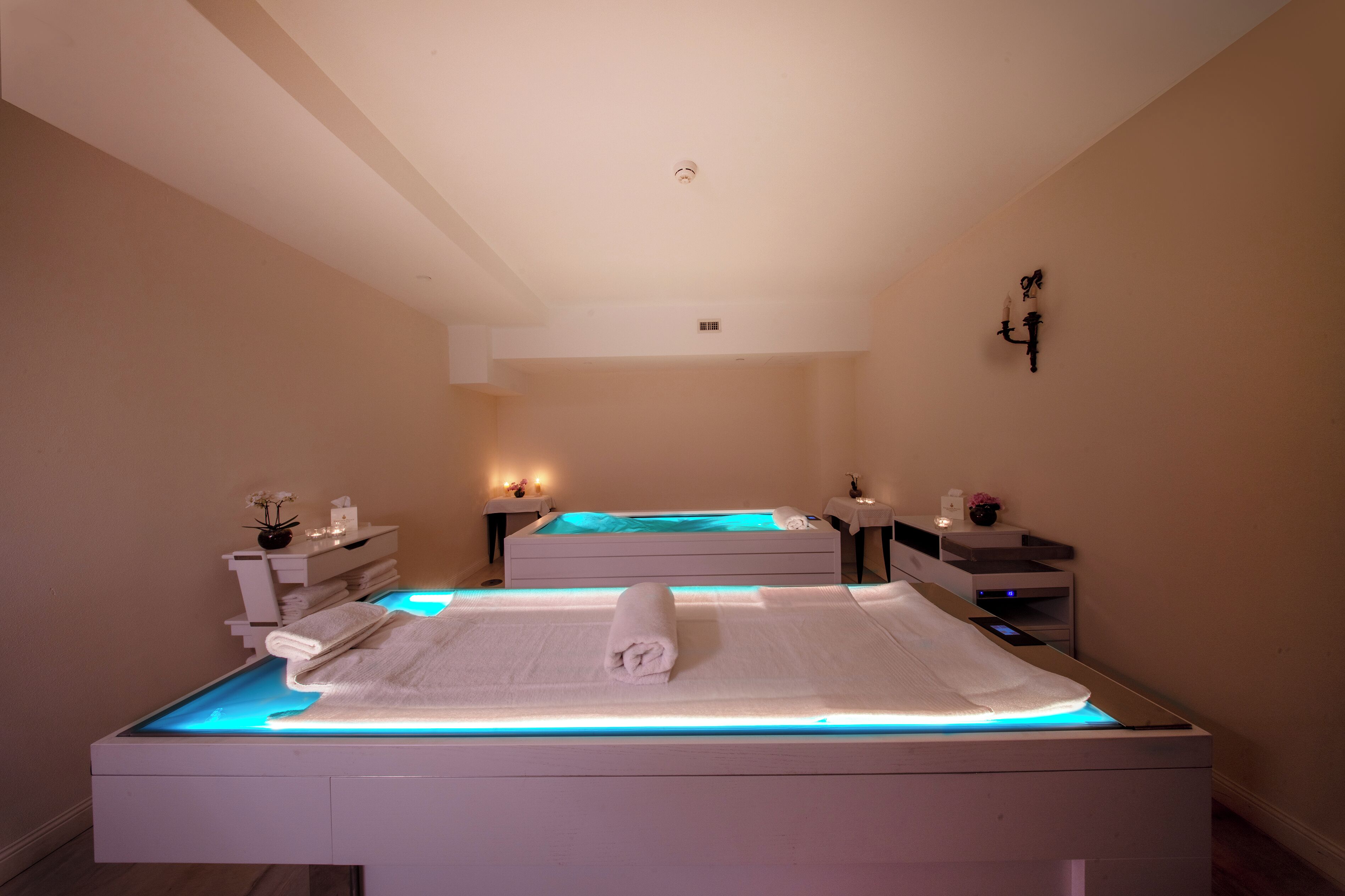 Ein Spa-Raum mit zwei Behandlungsbetten, jeweils mit einem Handtuch und einem kleinen Tisch mit einer Vase und Kerzen.