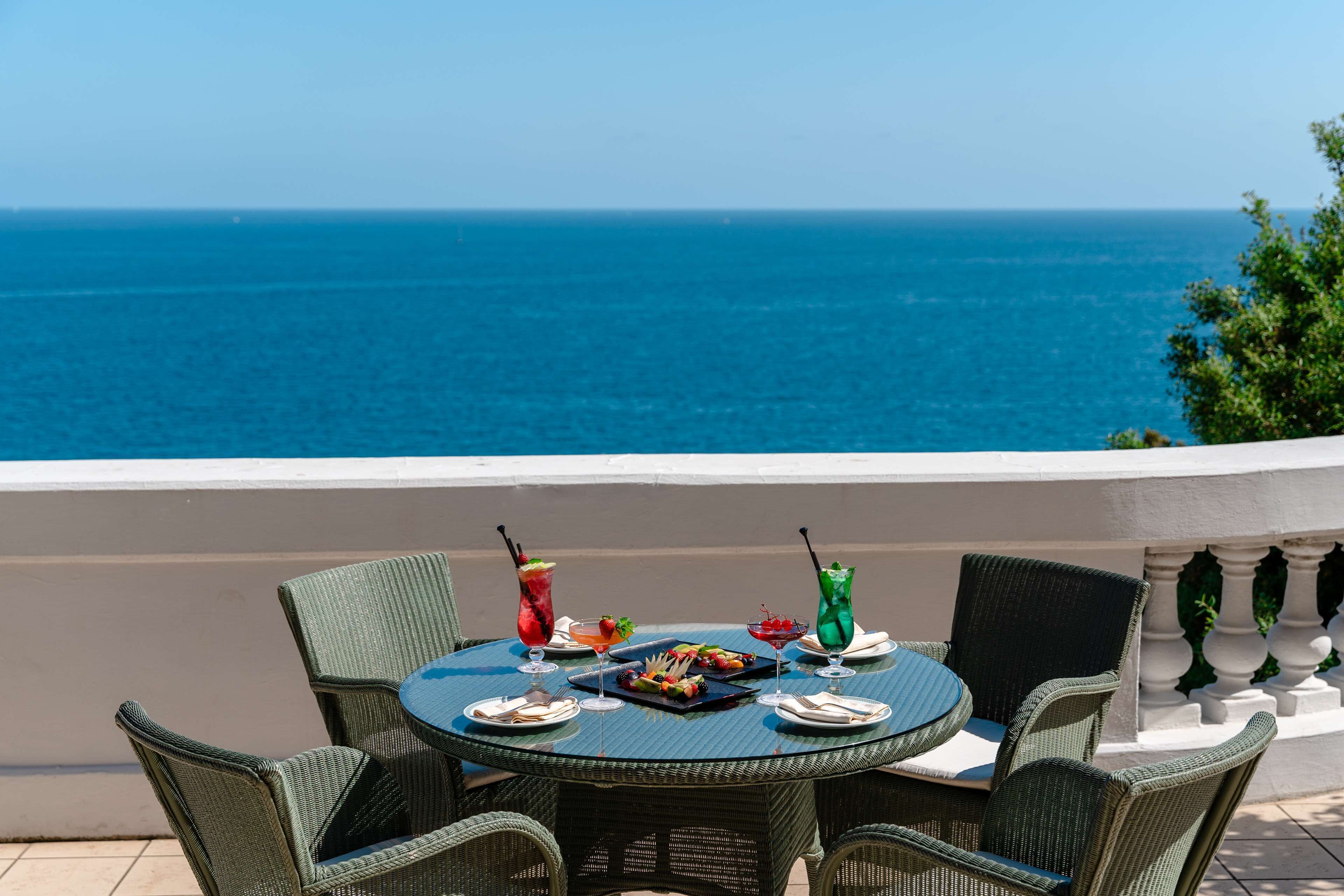 Ein runder Tisch mit Korbstühlen auf einem Balkon mit Blick auf das Meer.