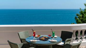 Ein runder Tisch mit Korbstühlen auf einem Balkon mit Blick auf das Meer.