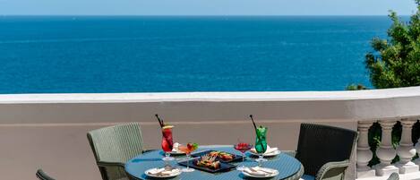 Una mesa redonda con sillas de mimbre en un balcón con vistas al mar.