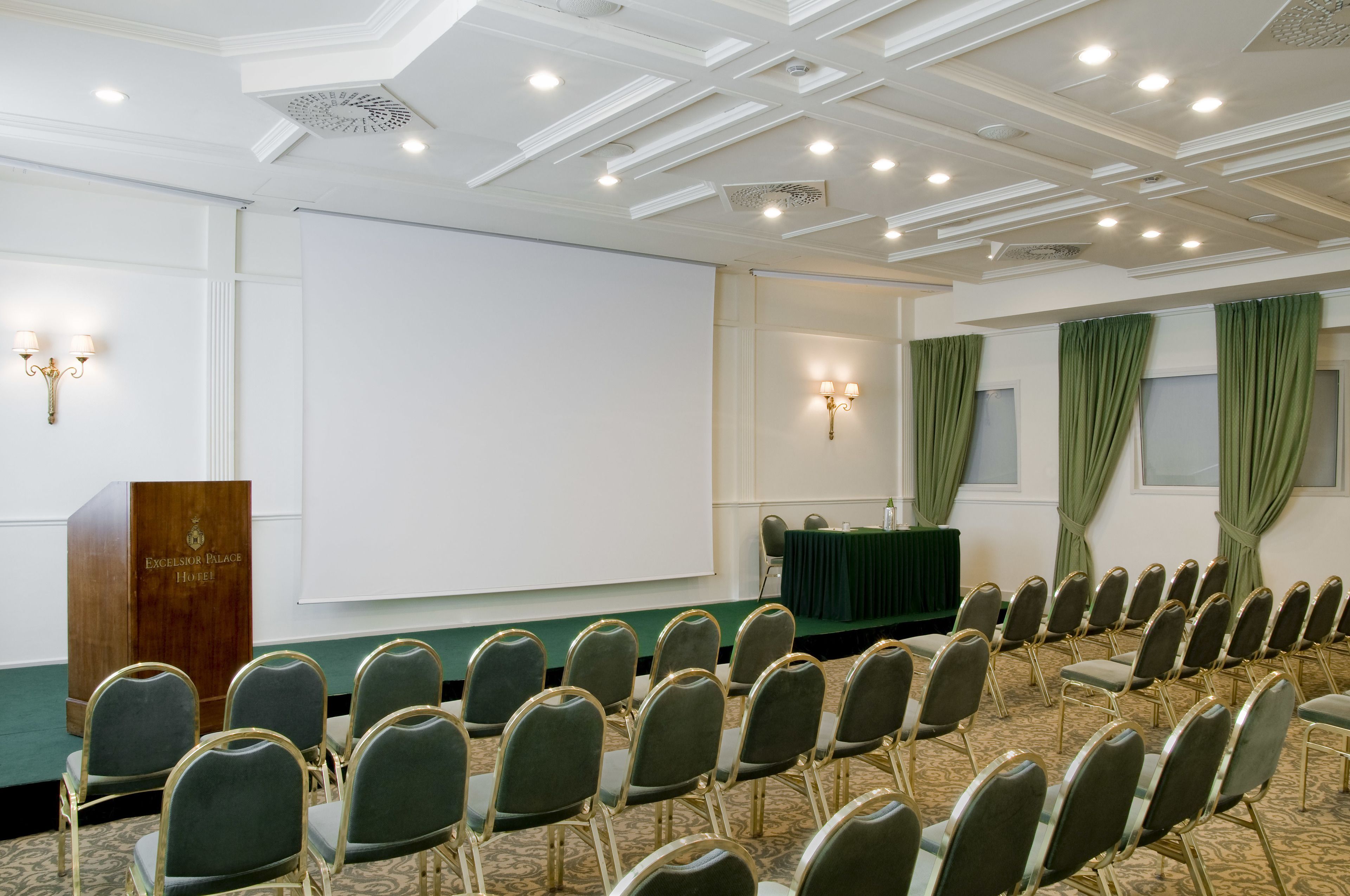 A conference room with rows of chairs, a podium, and a projection screen.