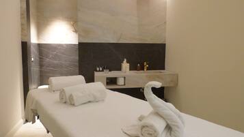 Un baño moderno con pared de mármol, un lavamanos con artículos de aseo y toallas sobre una estantería.