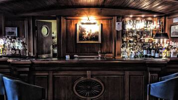 Angolo bar con pannelli in legno, un quadro appeso e diverse bottiglie sugli scaffali.