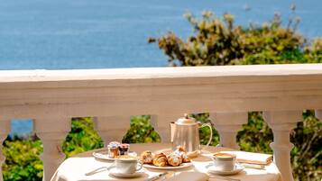 A table set for breakfast with a view of the sea, a white tablecloth, and striped cushions.