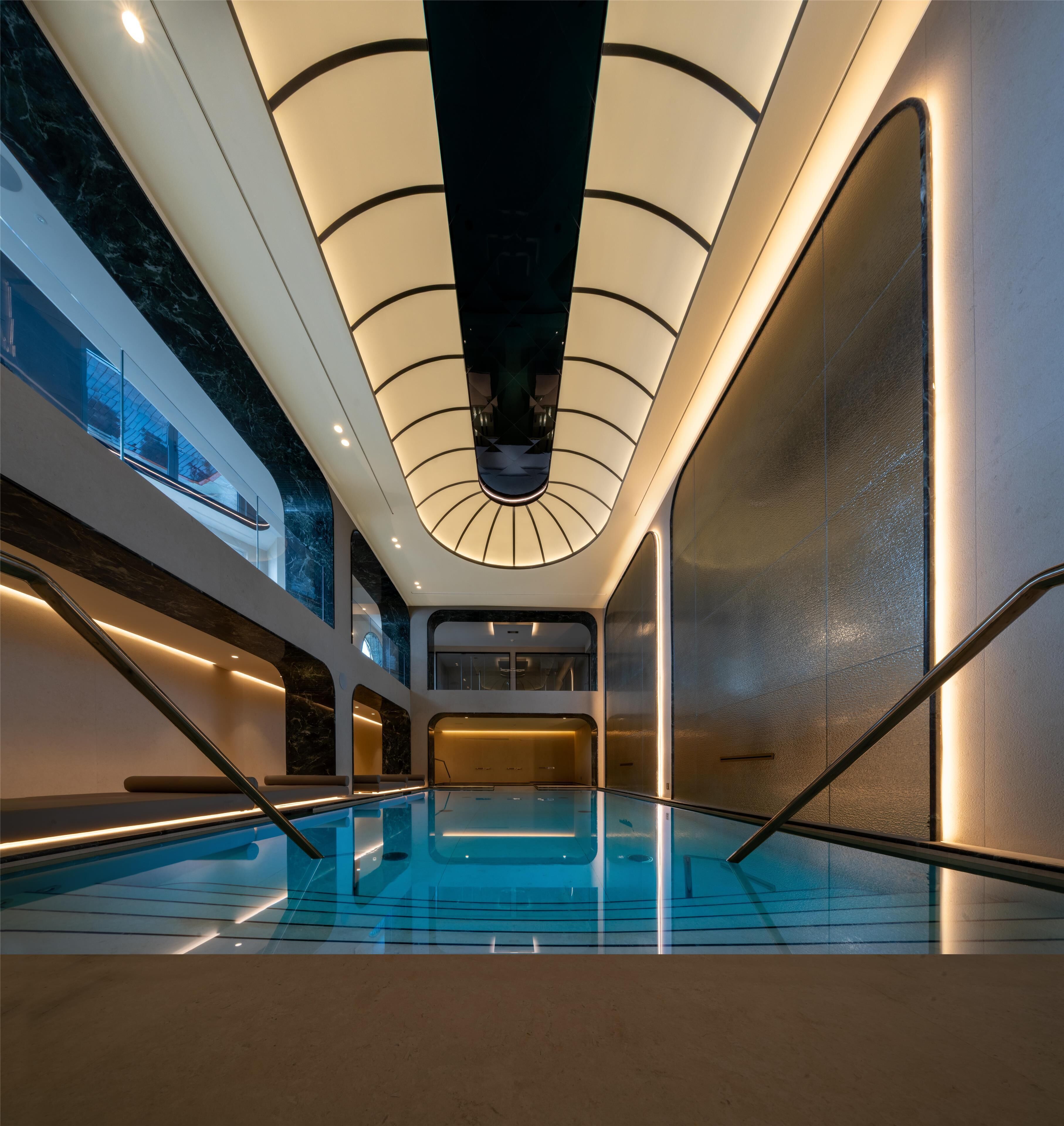 A modern indoor swimming pool with a glass ceiling and marble walls.