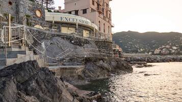 A coastal building named "EXCELSIOR" with a stone staircase leading to a terrace overlooking the sea.