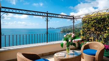 Un balcón con mobiliario de mimbre, una mesa de vidrio y vistas al mar.